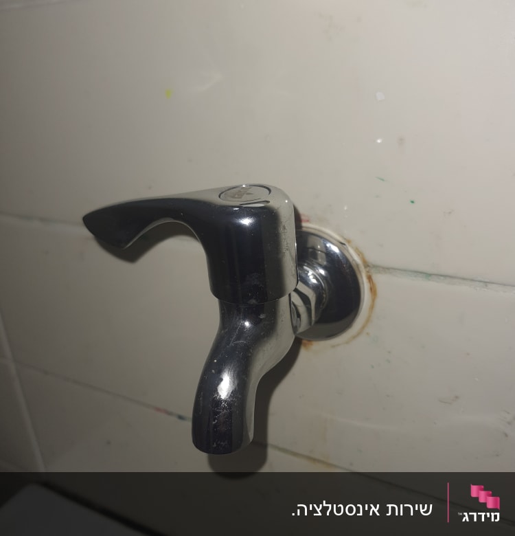 ברז מתכת מותקן על קיר אריחים לבנים